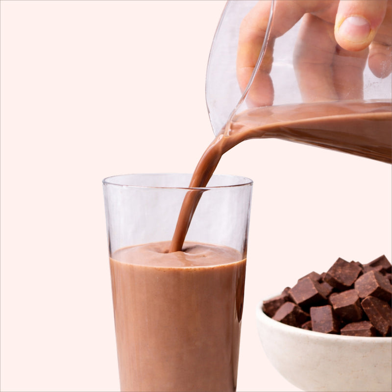 40738242232369  Chocolate milk being poured into a glass with chocolate pieces on a white background