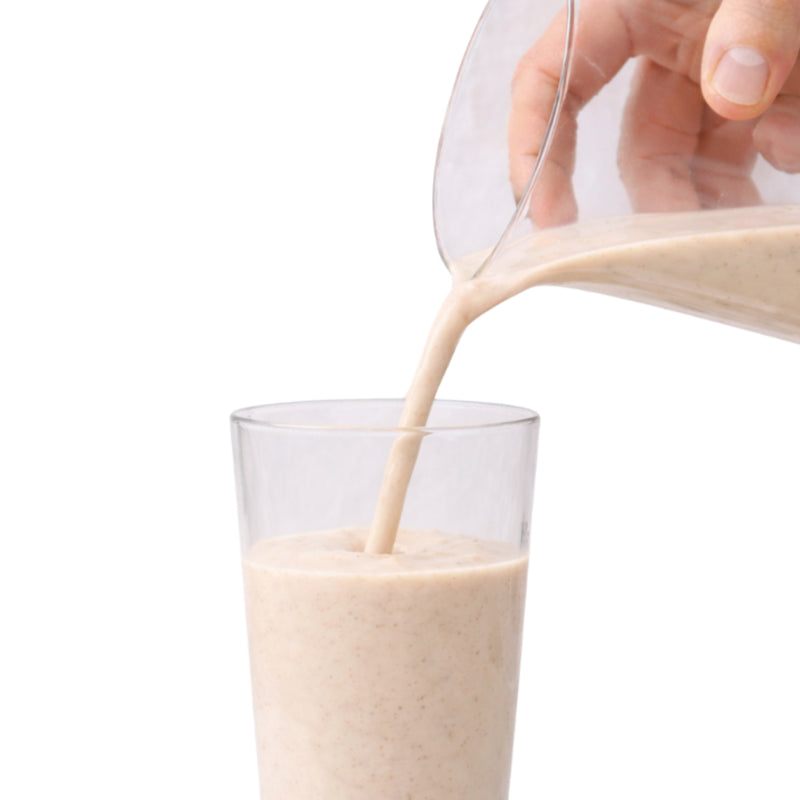 Hand pouring a creamy liquid into a glass against a white background